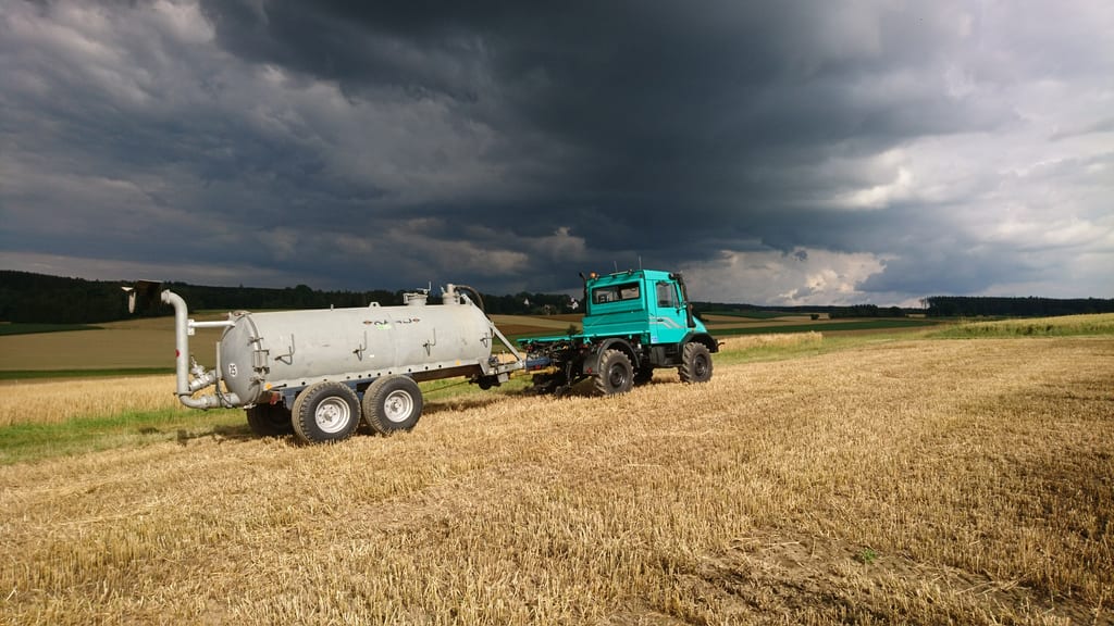 Unimog mit landwirtschaftlichem Anhänger auf einem Feld unter dramatischen Wolken